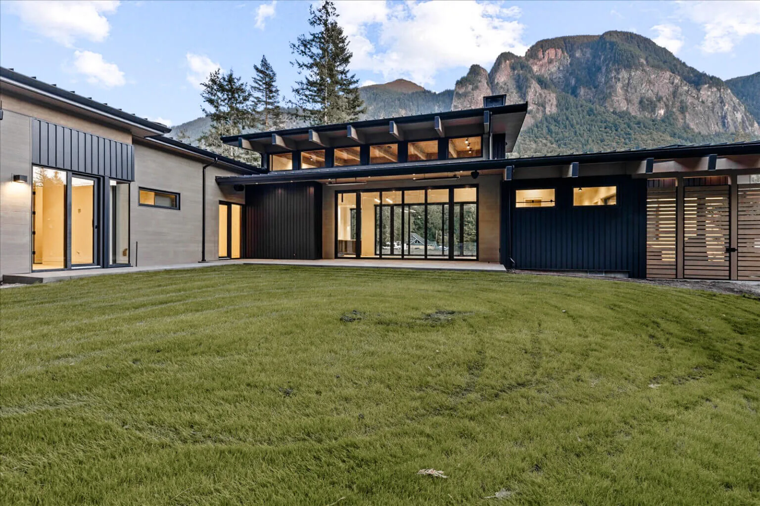 Exterior front view of Echo Ridge House showing black vertical siding, clerestory windows, and large glass doors with mountain scenery.