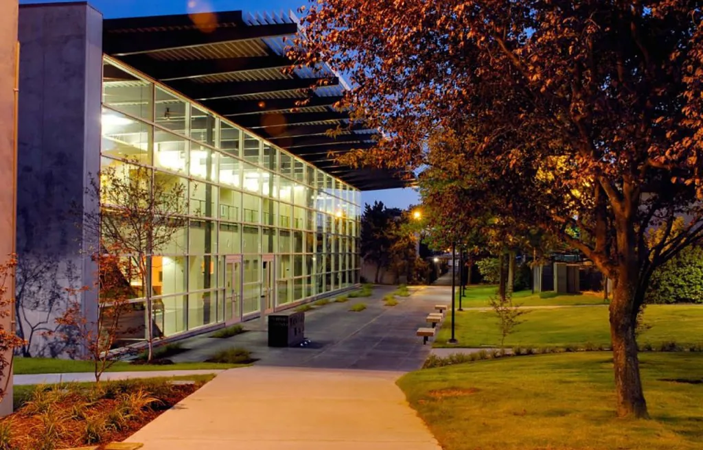 Exterior night view of a modern building featuring a glass curtain wall and metal sunshades with surrounding landscaping.