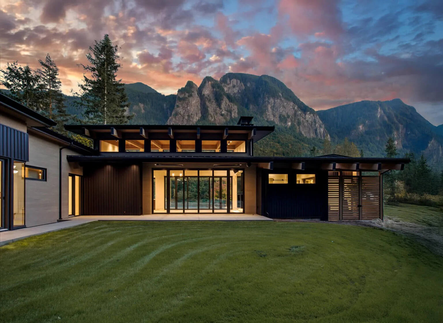 Rear exterior of Echo Ridge House features clerestory windows and a covered patio against a mountainous backdrop at dusk.