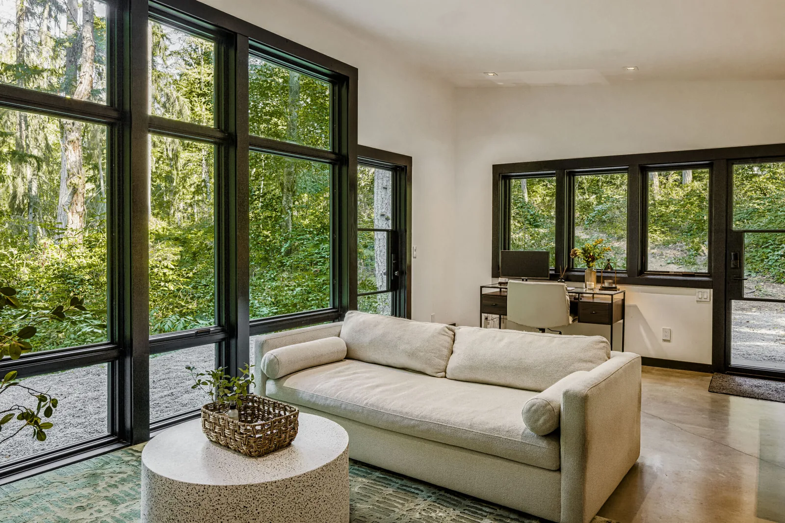 Living room and workspace with large black-framed windows offering forest views in the Evergreen Escape project.
