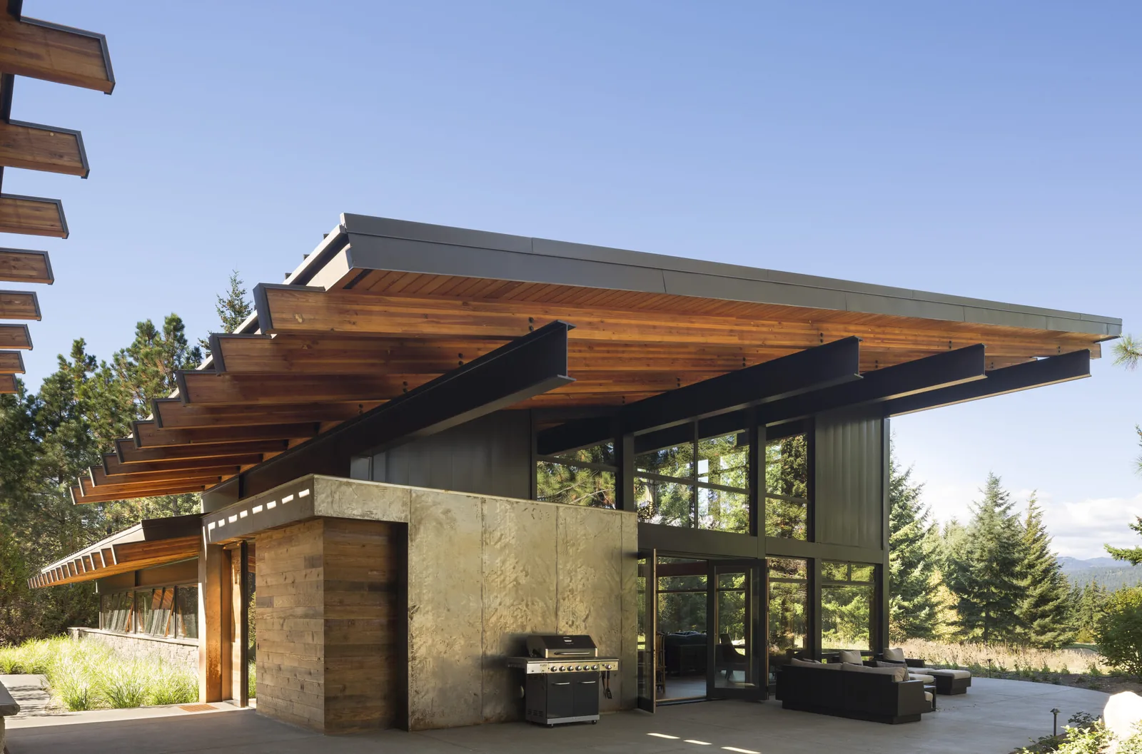 Modern house with cantilevered flat roof and floor-to-ceiling windows with outdoor sitting area.