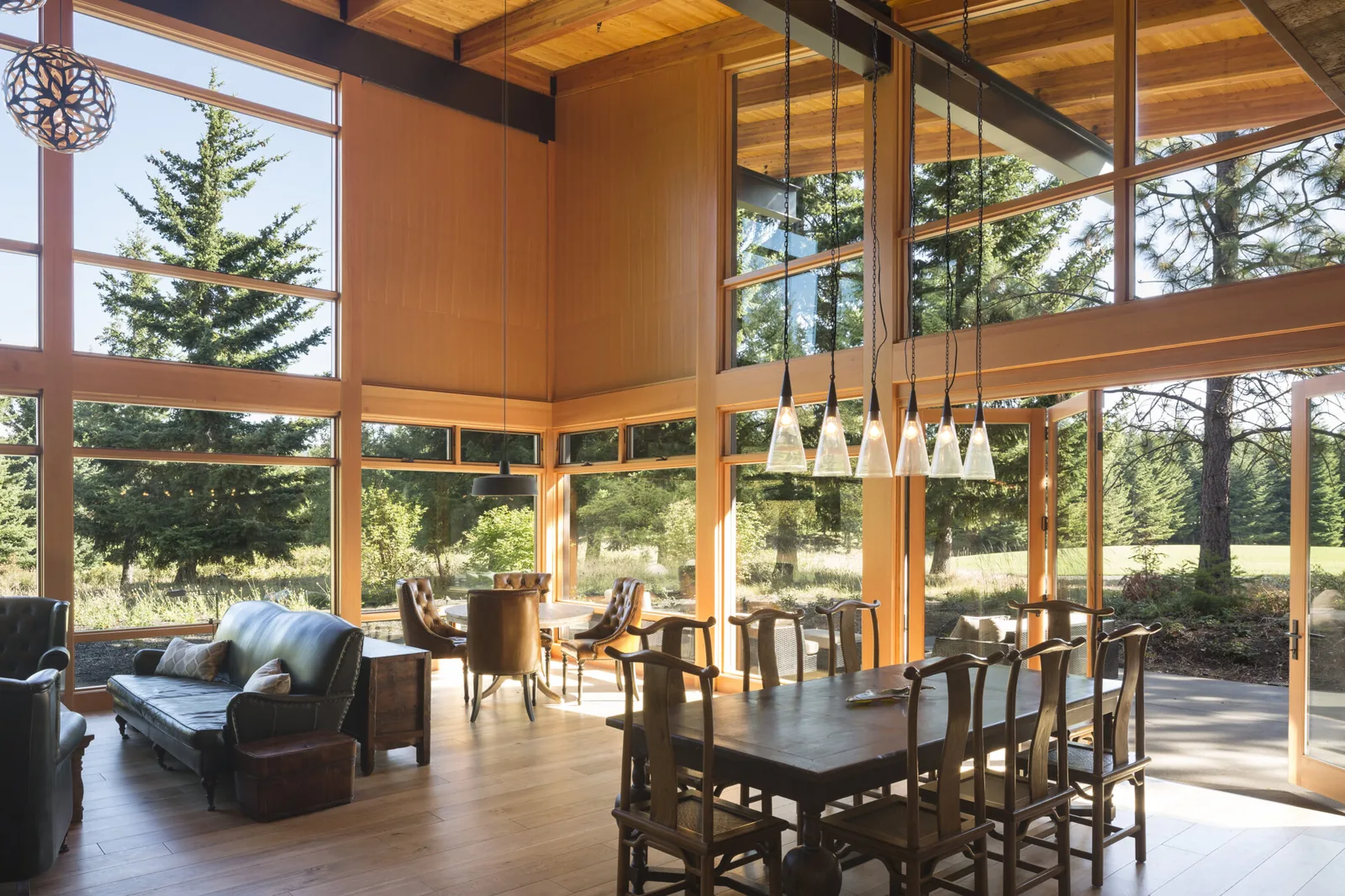 Open dining and living area with extensive floor-to-ceiling glazing and wood ceiling.