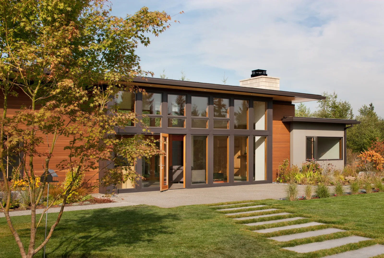 Exterior front view of a modern residential house with floor-to-ceiling windows and mixed wood and stucco siding.