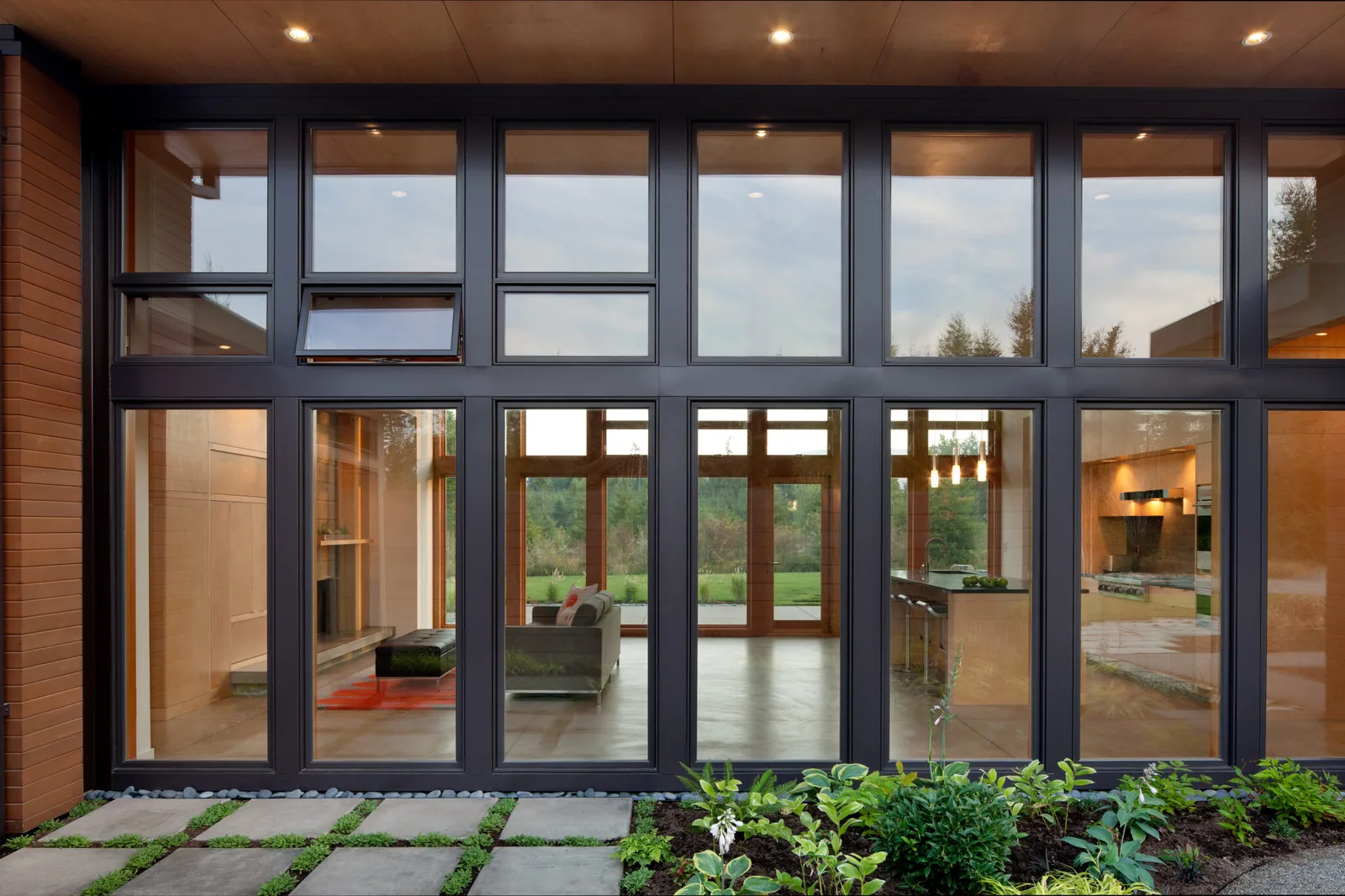 Exterior view of large floor-to-ceiling black-framed windows and sliding glass door looking into the living and kitchen areas.