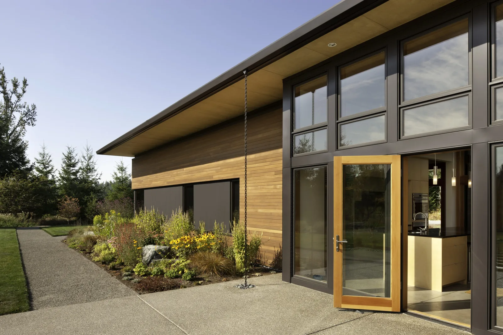 Exterior side view of a modern residence featuring wood siding and floor-to-ceiling glazing with an open wood-framed glass door.