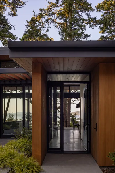 Entryway with wood siding and black window frames opens to views of the forest and water.