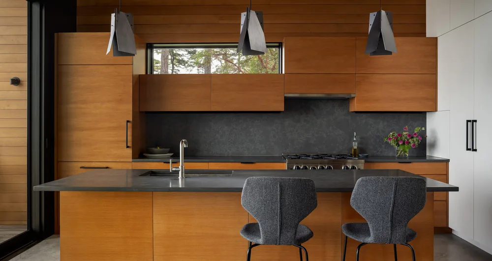 Kitchen featuring wood cabinets, concrete countertop island, and a black stone backsplash beneath a narrow horizontal window.