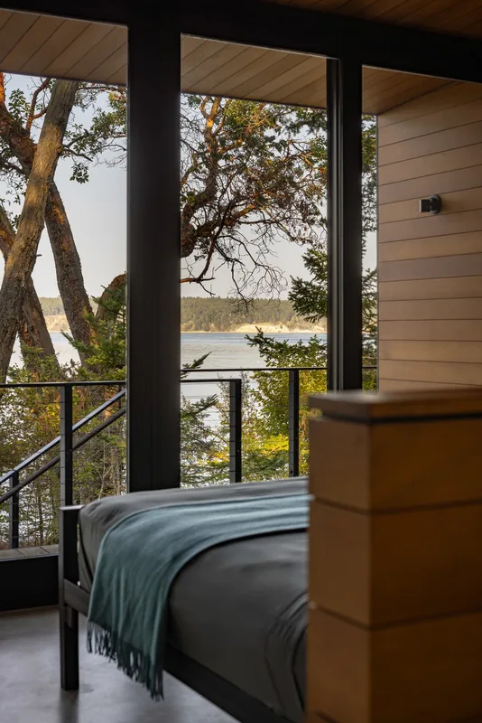 Bedroom with floor-to-ceiling glazing overlooking waterfront and trees.