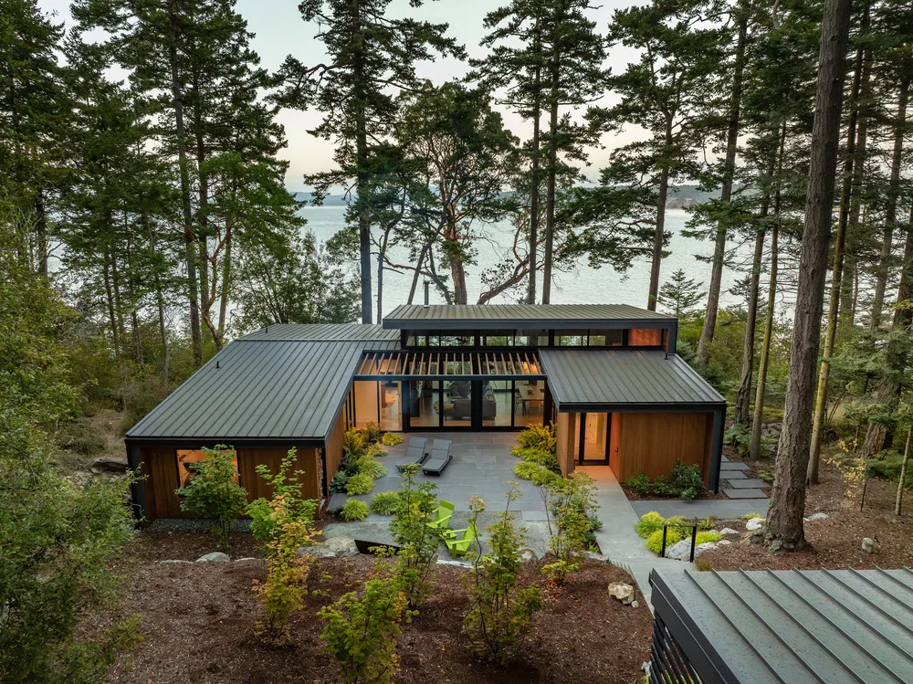Exterior rear view of a modern house with metal roofing and wood siding in a forested setting by water.