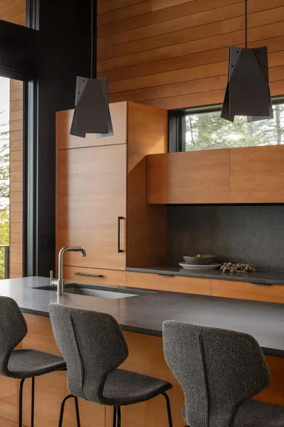 Modern kitchen featuring wood cabinetry, a gray countertop island, and pendant lighting over a breakfast bar.