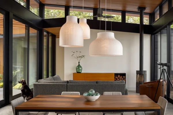 Modern living and dining room featuring floor-to-ceiling glazing and three large white pendant lights.