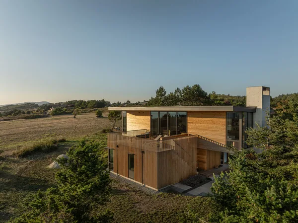 Two-story house exterior with wood siding and large glazing, located in a rural natural setting.