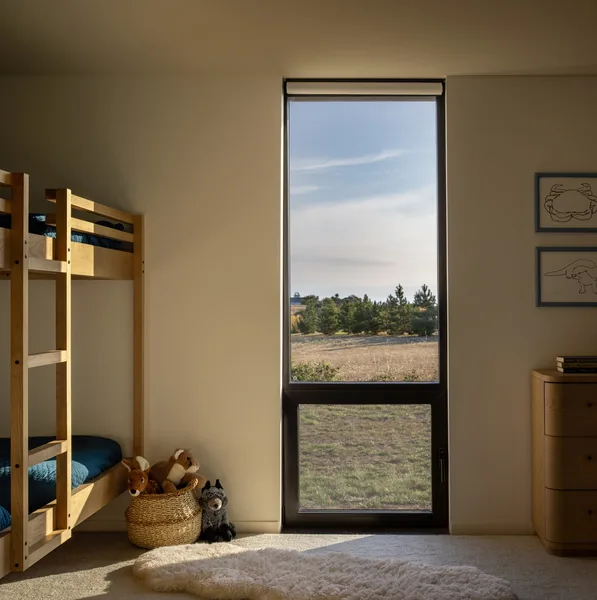 A bedroom interior featuring a wooden bunk bed and a tall narrow window overlooking an open field.