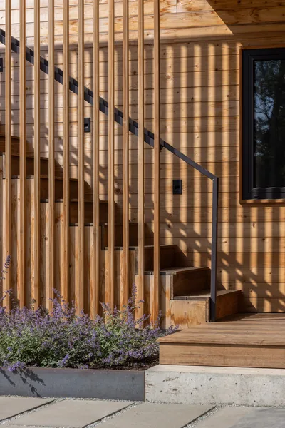 Exterior wooden stairs with vertical slats and metal handrail on a wood-paneled house facade