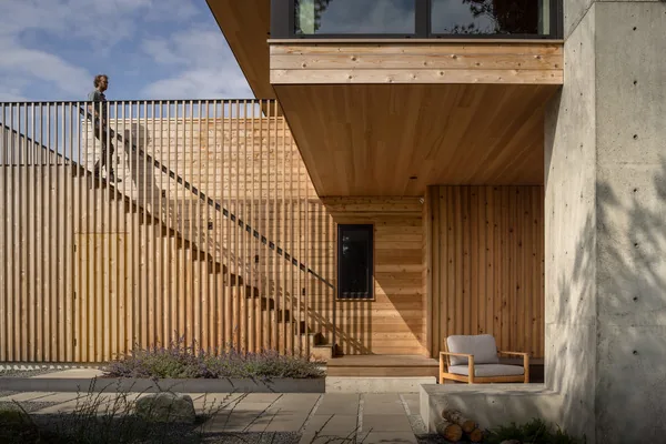 Exterior corner of a modern house with vertical wooden slats, concrete walls, and an exterior staircase with wood railing.