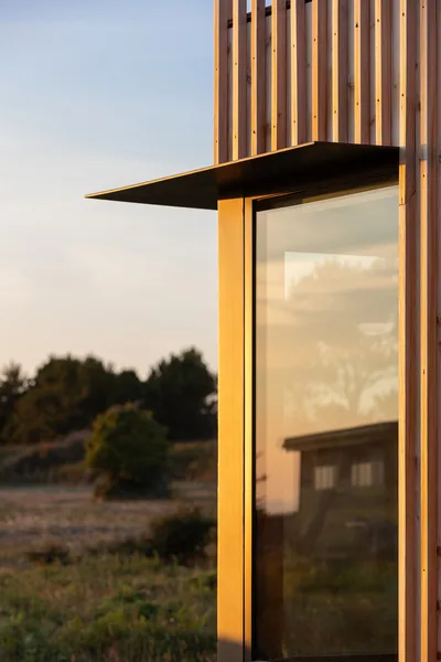 Detail of vertical wood siding and large glass window with a flat metal canopy at a building corner.