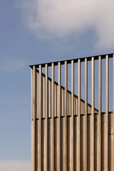 Detail of a wooden vertical slat architectural screen with a diagonal shadow cast across it.