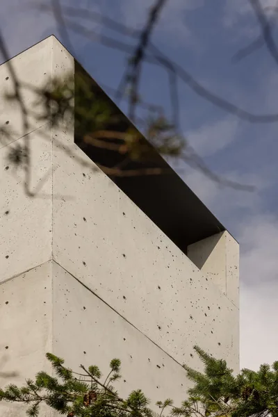 Concrete exterior corner detail with recessed black metal panel under the roof.