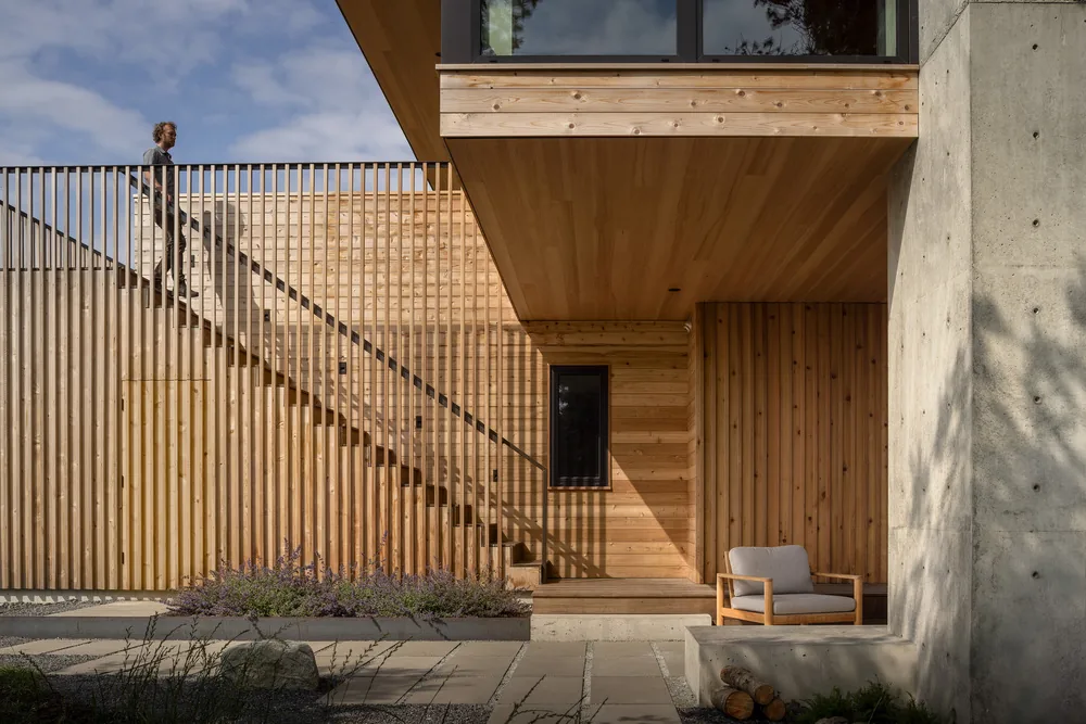 Modern exterior deck with vertical wood slat railing, concrete wall, and wood siding under a covered ceiling.