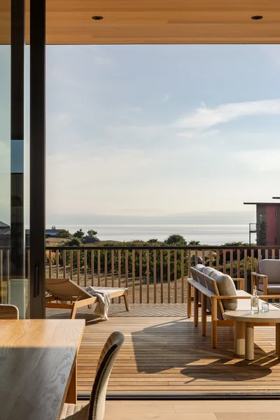 Interior space opens to a wooden deck with outdoor furniture and a scenic view beyond.