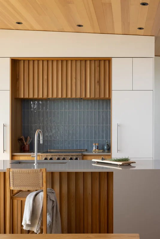 Kitchen with vertical wood slat cabinetry, blue tile backsplash, and integrated cooktop.