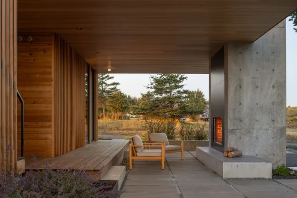 Covered patio features a concrete fireplace, wood plank flooring, and seating with a view of the landscape.