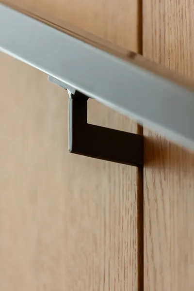 Detail view of a minimalist stainless steel handrail attached to a wood-paneled wall.