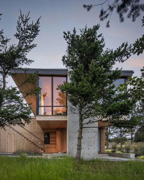 Exterior front view of a modern house featuring floor-to-ceiling glazing, wood siding, and exposed concrete walls.