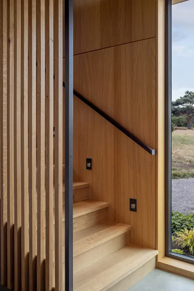 Staircase with wood paneling and vertical wood slats beside a large window overlooking a natural outdoor area.