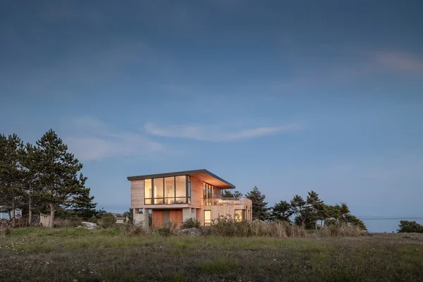 Modern two-story house with extensive glazing set in a natural grassy landscape.