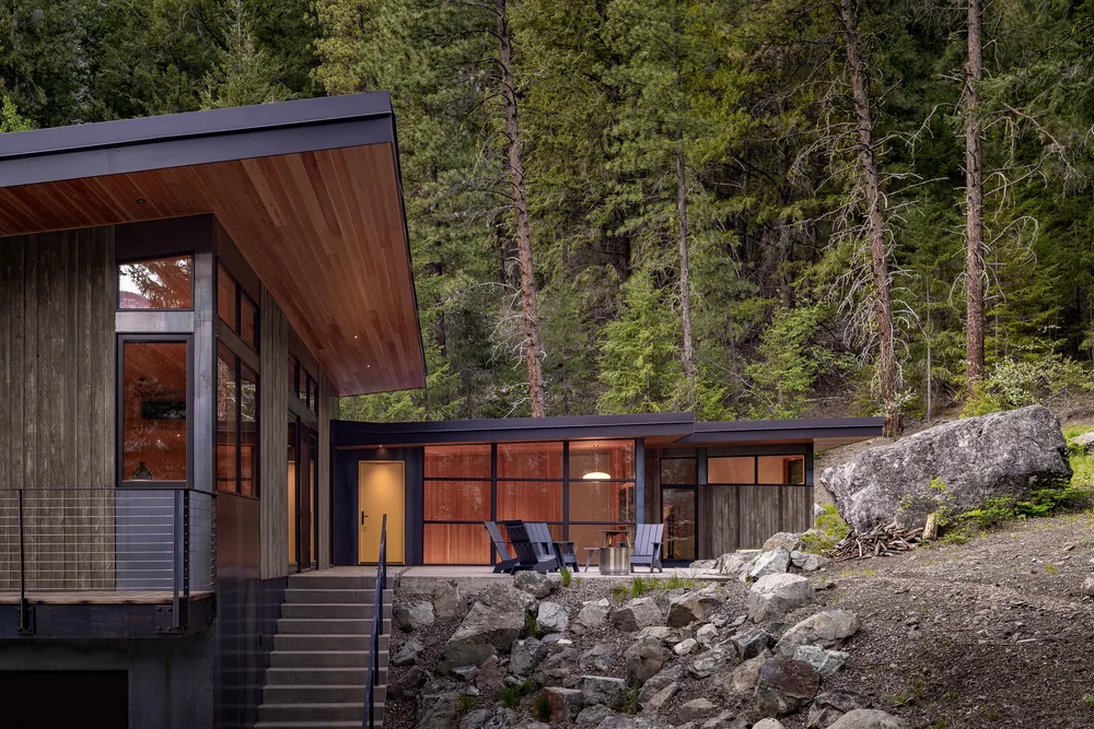 Exterior front view of a modern hillside house featuring wood siding, floor-to-ceiling glazing, and a flat roof.