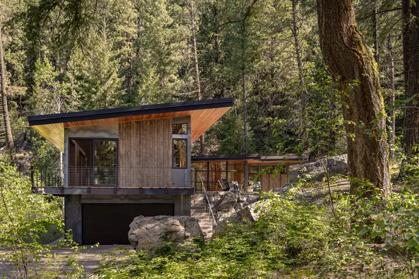 Modern hillside house with concrete base, wood cladding, large windows, and sloped roof.