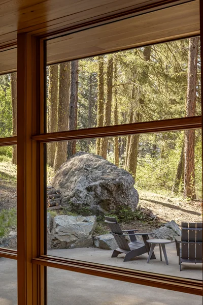 Outdoor seating area seen through wood-framed windows with natural stone elements and forest surroundings.