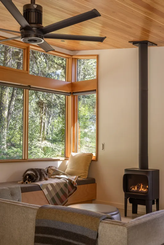 Living room corner with large corner windows, wood ceiling, black ceiling fan, and a gas stove.