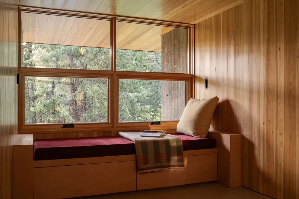 Cozy window seat with wood panel walls and a view of trees through a large framed window.