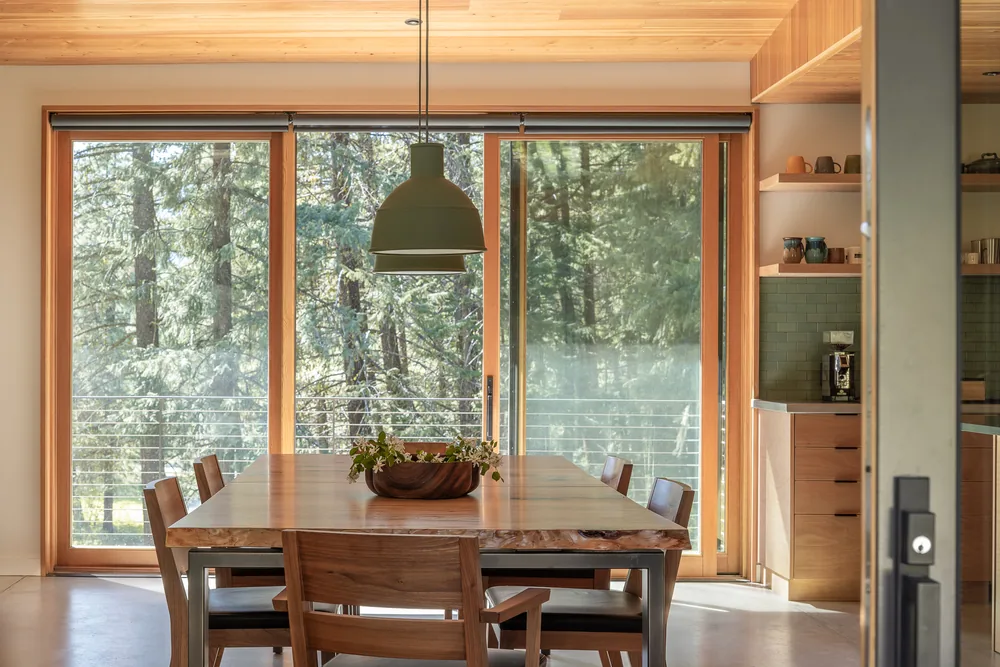 Dining room with floor-to-ceiling sliding glass doors overlooking a forested exterior.
