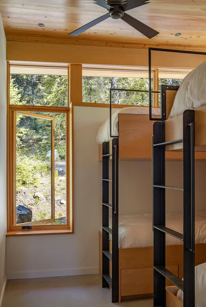 Bedroom with bunk beds and a floor-to-ceiling wood-framed window opening to a forested exterior.