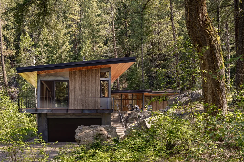 Exterior front view of a modern hillside house with a sloped roof and mixed wood and concrete facade.