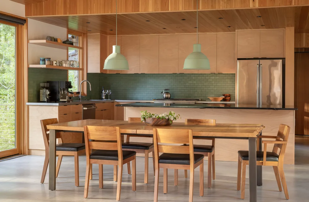 Kitchen and dining area featuring wooden cabinetry, green subway tile backsplash, and pendant lighting.