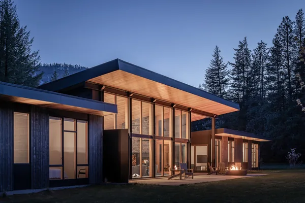 Twilight exterior of a modern flat-roofed house with extensive glazing and outdoor seating areas.
