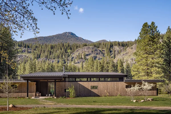 Single-story modern residence with horizontal wood siding and metal roof in a natural mountain setting.