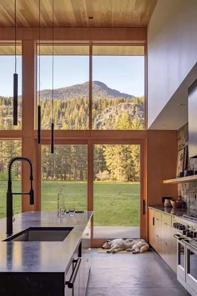 Kitchen interior with floor-to-ceiling windows framing a mountain and forest landscape.