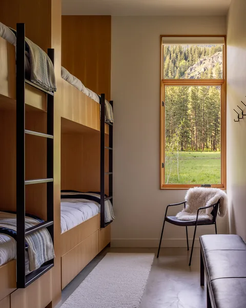 Interior view of a narrow bedroom with built-in bunk beds and a window looking out onto a meadow and forest.