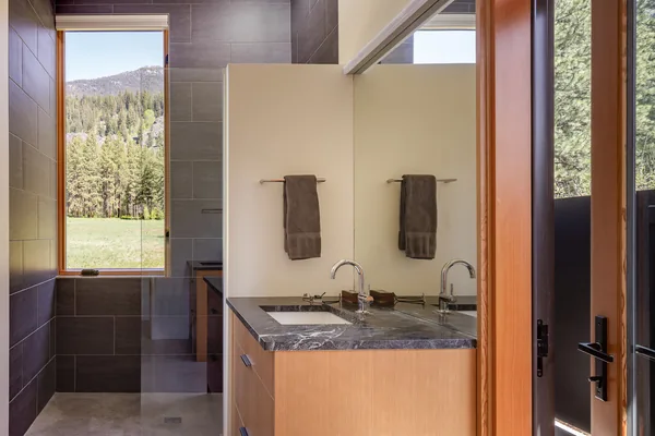 Modern bathroom featuring a wood vanity with black stone countertop and a walk-in glass shower with window.