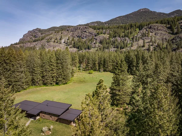 Single-story house with flat roof set in a meadow with surrounding forest and mountains.