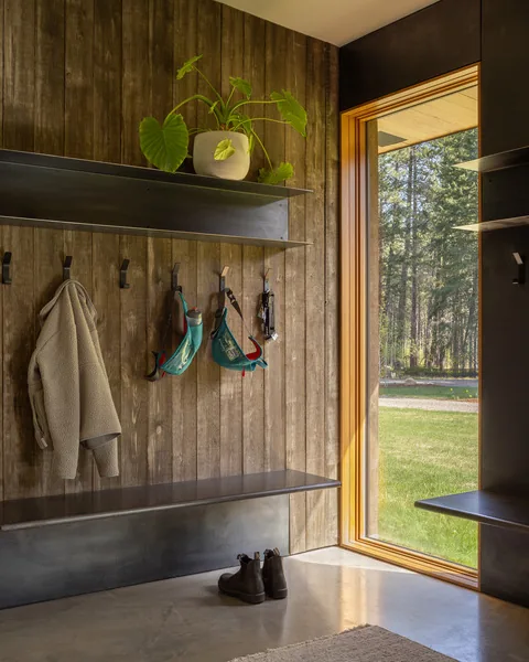 Mudroom area featuring vertical wood paneling, metal shelving, and a large wood-framed window looking outside.