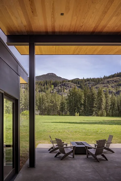 View from a covered patio with wooden ceiling and steel supports toward a meadow and hillside.
