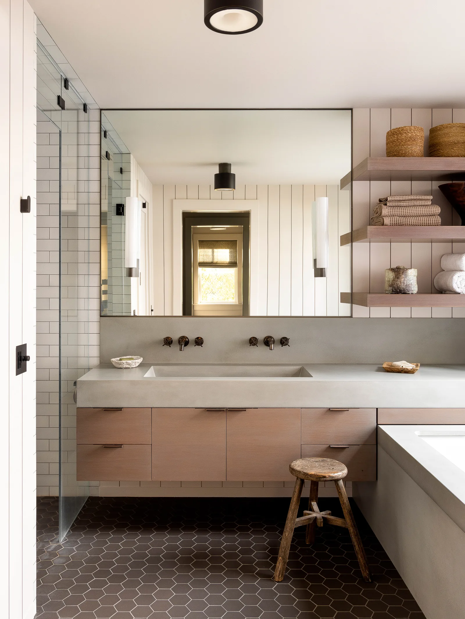 Bathroom featuring a floating wooden vanity with concrete countertop, a large mirror, open wood shelves, and hexagonal floor tiles.