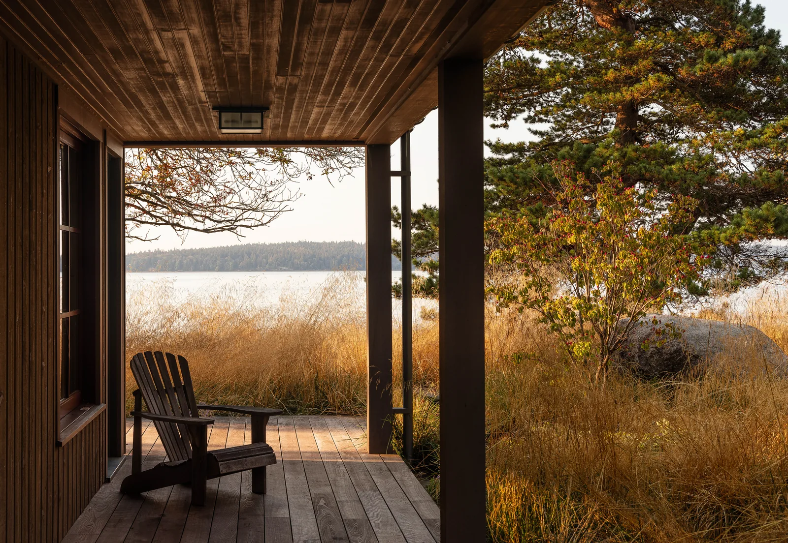 Wooden porch with Adirondack chair overlooking a natural landscape and water.