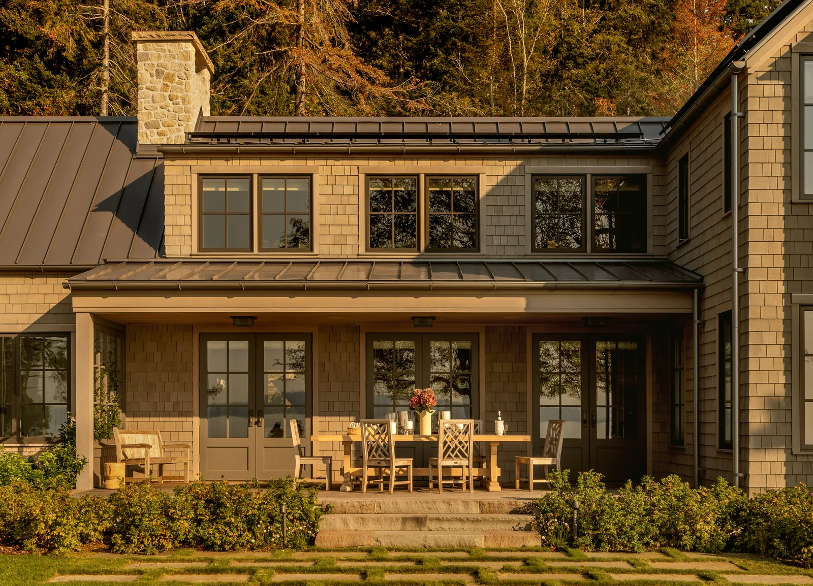 Rear exterior view of a two-story shingle-style house with a covered patio and outdoor dining set.